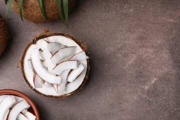 Coconut pieces in nut shell on brown table, flat lay. Space for text