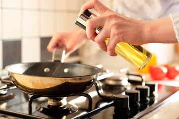 Vegetable fats. Woman sprinkling oil into frying pan on stove in kitchen, closeup