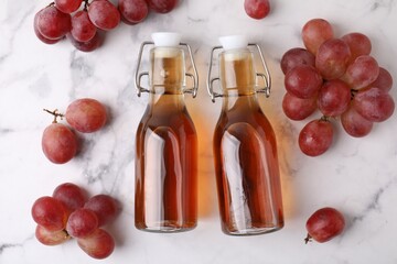 Wine vinegar in glass bottles and grapes on white marble table, flat lay