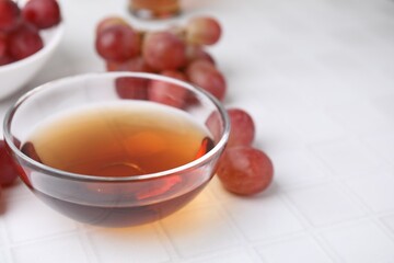 Wine vinegar in glass bowl and grapes on white table, closeup. Space for text