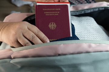 female hands packing travel bag, German international passport for vacation, emigration, excitement...