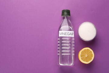 Eco friendly natural cleaners. Vinegar in bottle, cut lemon and bowl of soda on purple background,...