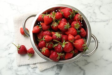 Metal colander with fresh strawberries on white marble table, top view