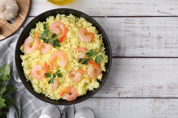 Delicious risotto with shrimps and parsley in bowl on white wooden table, flat lay. Space for text