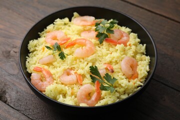 Delicious risotto with shrimps and parsley in bowl on wooden table, closeup