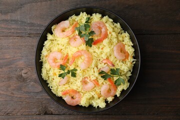 Delicious risotto with shrimps and parsley in bowl on wooden table, top view