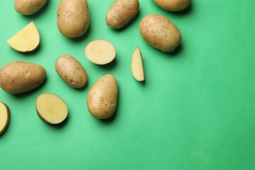 Fresh raw potatoes on green background, flat lay. Space for text