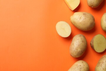 Fresh raw potatoes on orange background, flat lay. Space for text