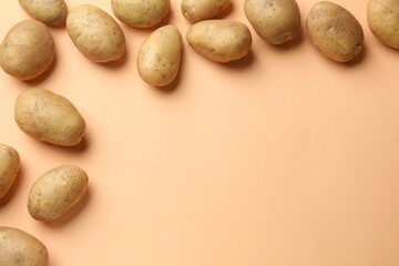 Fresh raw potatoes on pale orange background, flat lay. Space for text