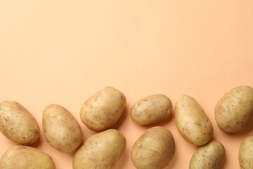 Fresh raw potatoes on pale orange background, flat lay. Space for text
