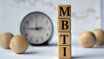 MBTI - acronym on wooden cubes on graph, clock and wooden balls background.