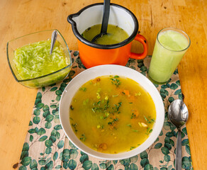 Vegetable broth in white plate and in orange pot, cucumber salad and smoothie on table.