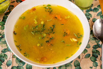 Dense vegetable broth with herb in white plate, spoon .