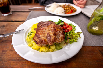 Juicy pork steak with light potato salad and vegetable in first plate, rice, second meal on table.
