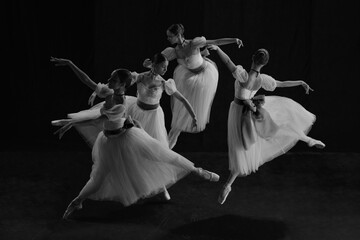 Black and white photo of young female ballet dancers in synchronized motion, their white tutus...