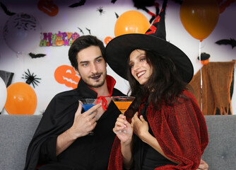 The couple is happily drinking wine on Halloween night party, wearing dressed carnival Halloween costumes and makeup posing with Halloween background. Halloween holiday party concept