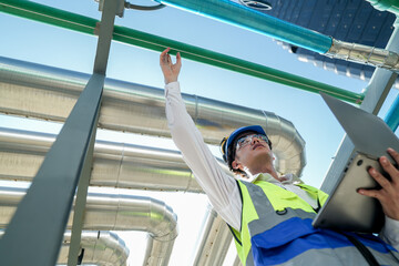 Industrial engineer adjusting pipeline valve with radio communication on construction site. Engineer on urban construction site using radio to coordinate with team on a sunny industrial rooftop.