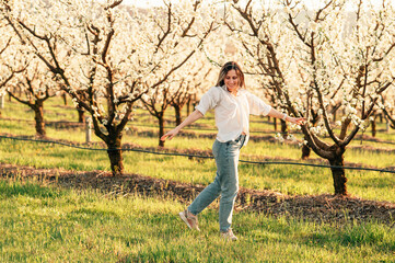 Handsome young cheerful woman in jeans is dancing through an almond orchard.