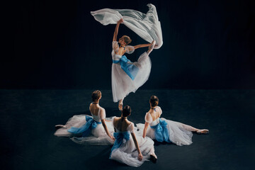 One ballerina dressed in flowing white dress performing with fabric in motion and her partners...