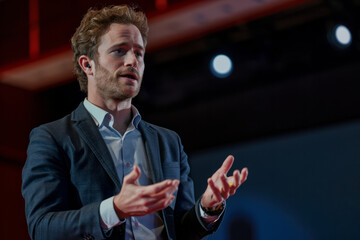 A Caucasian business executive, delivering a TED talk on the future of work and the importance of adaptability in the face of technological disruption, sharing insights and strategies to thrive in an