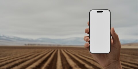 Hand holding a phone with a blank screen against a cultivated field backdrop