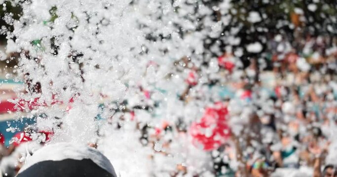 Automatic foam machine shoots with froth at poolside foam party in daytime. Mechanical equipment for fun holidays. Wet fluffy substation producing slow motion