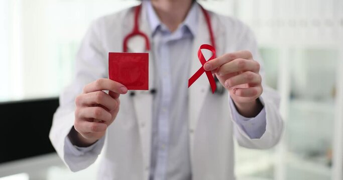 Doctor in white lab coat holds red ribbon and condom in hands. International symbol of AIDS and HIV awareness and health protection slow motion