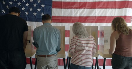 Four voters casting ballots at election booths, seen from behind. Wide shot with faces mostly...