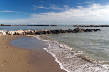 Tranquil beach scene with clear waters and sandy shore, flanked by rocky barriers under an expansive sky, ideal for serene nature themes