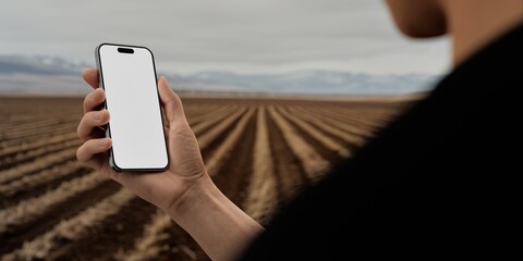 Hand holding a phone with a blank screen against a cultivated field backdrop