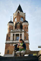 Young woman with Beautiful black dog sits and poses near Gardos Tower -Millenium Tower- in...