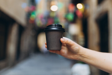 Woman gives paper black coffee cup or tea on urban background. Take away or delivery concept. Copy space. Place for your text on mug, mockup.