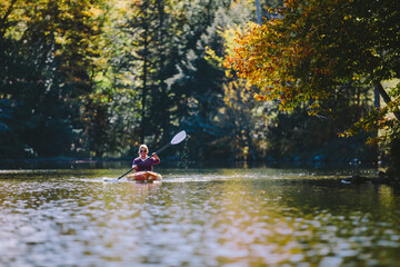 Woman kayaking on a lake during peak autumn foliage smiling with blonde hair and paddle.