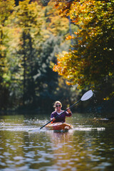 Woman kayaking on a lake during peak autumn foliage smiling with blonde hair and paddle.