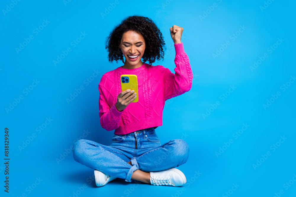 Poster Full size photo of pretty young girl sit floor hold device winning wear trendy pink outfit isolated on blue color background