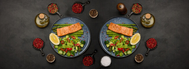 Healthy lunch with grilled trout with asparagus and fresh tomato and cucumber salad, a lemon slice. Food on a blue round plate