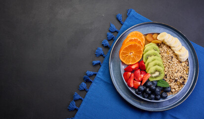 Granola with strawberries, kiwi, banana and blueberries in a round plate on a black table. Healthy and tasty food, top view