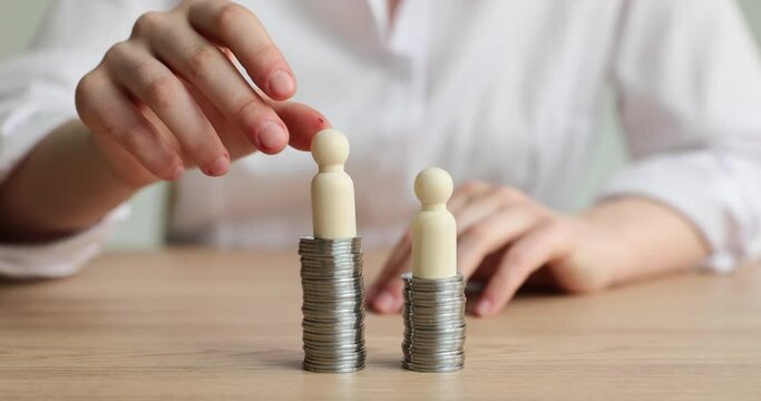 Female person in white shirt puts wooden figurines on towers made of coins sitting at desk. Concept of earning money by company members slow motion