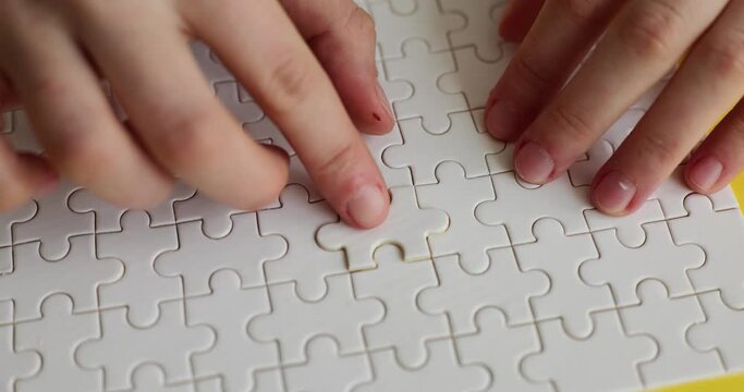Female hands insert missing piece into white puzzle on yellow background. Finding perfect business strategy. Successful combination of solutions slow motion