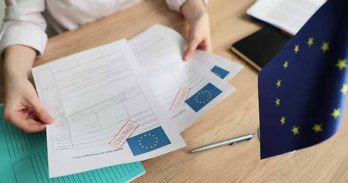 Woman examines visa application forms with Approved stamp sitting at wooden table in office. Consular officer checks documents sitting at workplace slow motion