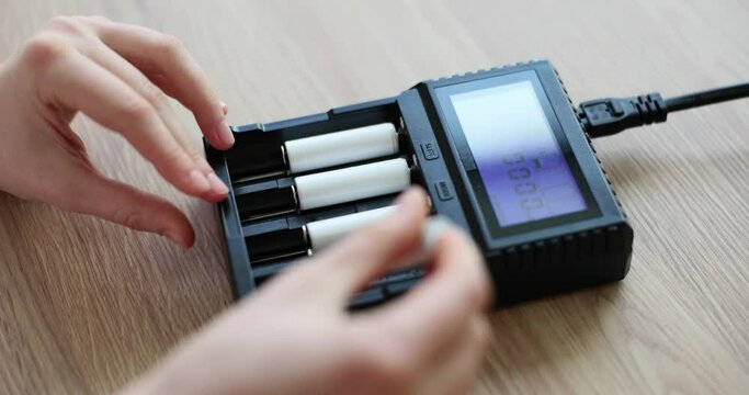 Woman hands insert cells for battery into charger. Device for increasing battery power on wooden desk. Support for operation of electronic devices slow motion