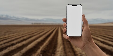 Hand holding a phone with a blank screen against a cultivated field backdrop