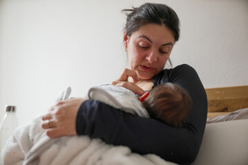 Mother nursing her newborn, eyes closed, showing the emotional and physical demands of early...