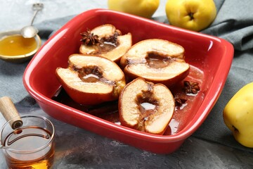Tasty baked quinces with honey in dish on grey textured table, closeup