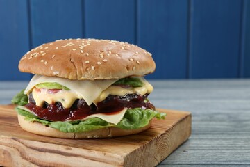 Tasty homemade cheeseburger with lettuce on grey wooden table, closeup. Space for text