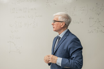 Mature man stands at a white board with written formulas. 