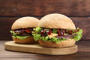 Board with delicious cheeseburgers on wooden table, closeup