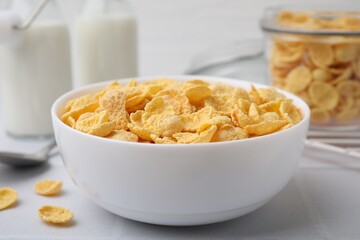 Tasty crispy corn flakes in bowl on white table, closeup. Breakfast cereal