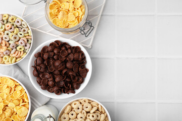 Different delicious breakfast cereals and milk on white tiled table, flat lay. Space for text