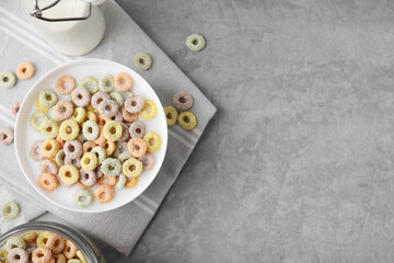 Tasty colorful cereal rings and milk in bowl on grey table, flat lay. Space for text